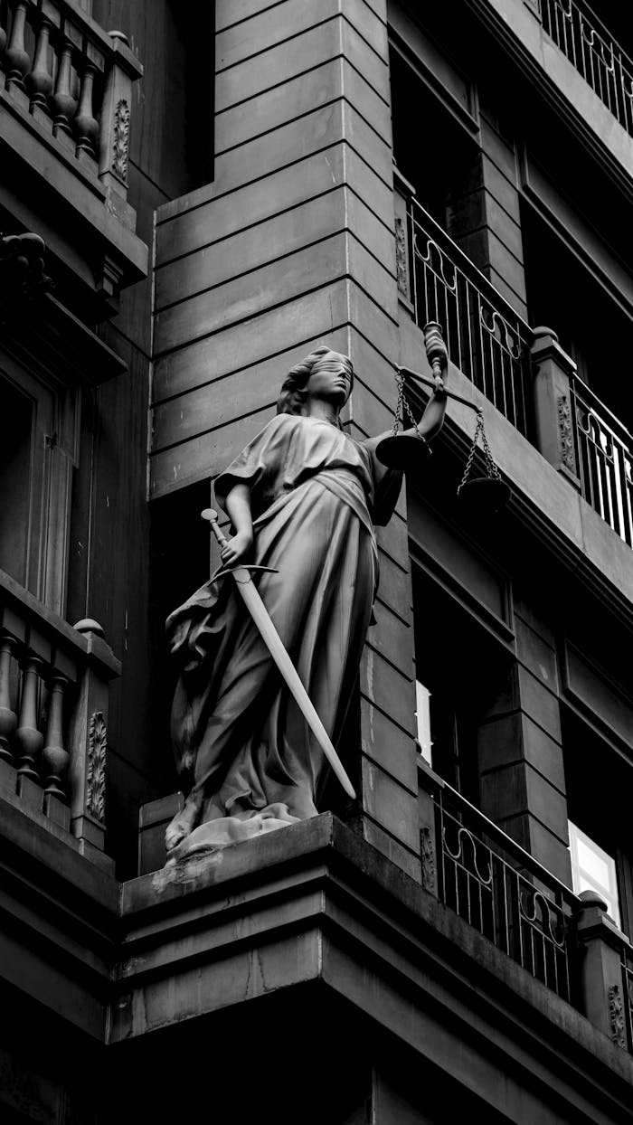 why-choose-us A dramatic black and white photo of a justice statue holding a sword and scales.